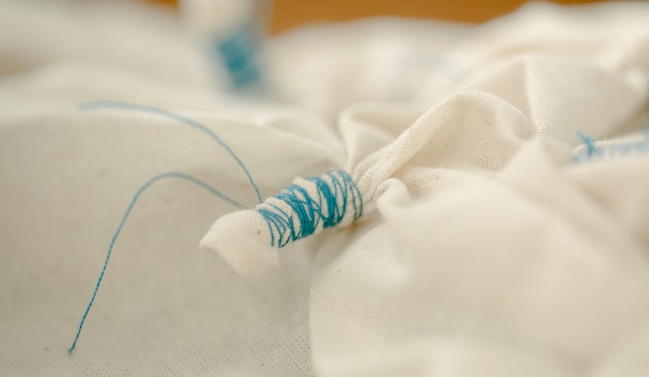 Closeup of white draped fabric tied with blue thread during creating traditional Japanese shibori pattern in workshop