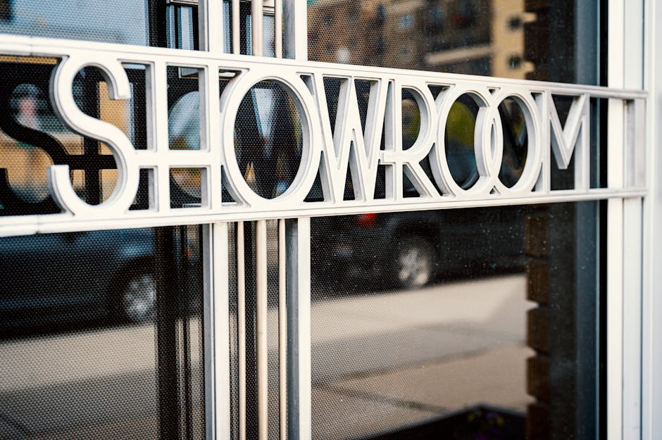 Store with Showroom title on glass window reflecting tiled pavement and road with cars behind multistage building in town in daylight