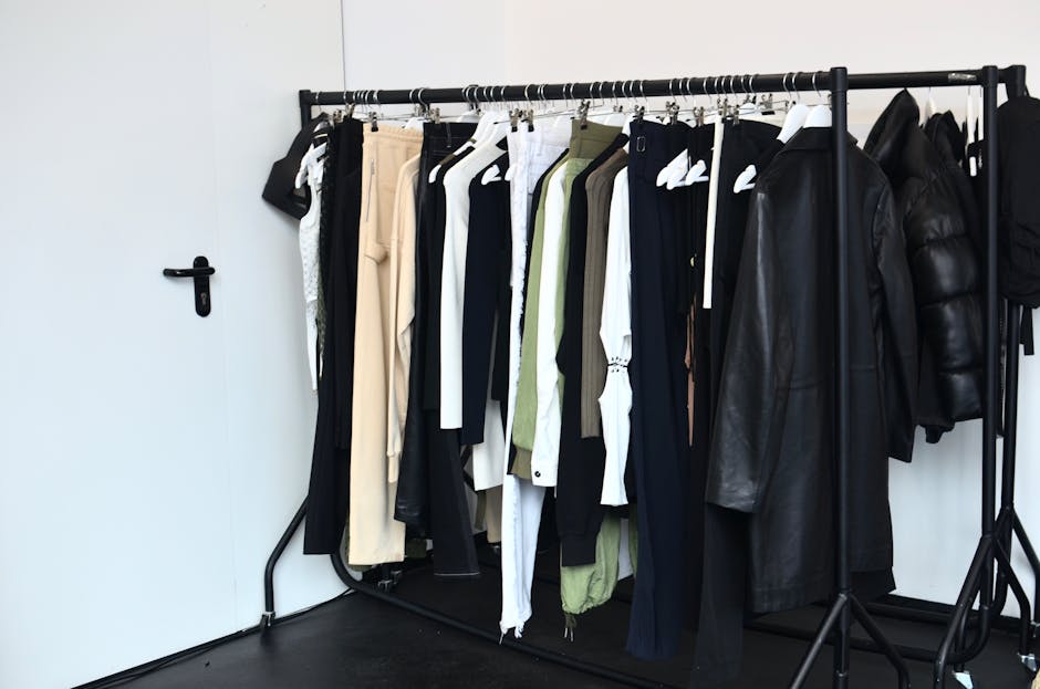Collection of stylish clothes and outerwear on hangers hanging on rack near door in light wardrobe room in modern studio
